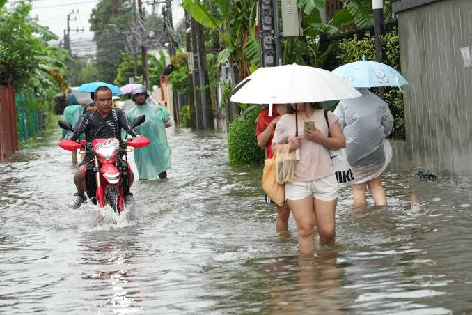 Flooded street with residents wading through water in central Thailand