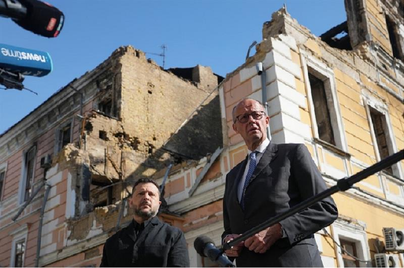 Chancellor Friedrich Merz and President Volodymyr Zelenskiy standing in front of a damaged building in Kyiv