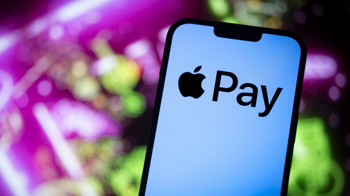 A person holding an iPhone showing Apple Wallet at a checkout terminal