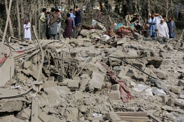 Rubble of a house damaged in an airstrike with people standing nearby